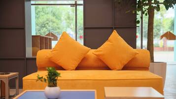 A modern living room with a sofa and two matching cushions, a small table with a plant, and a view of a tree and buildings outside.