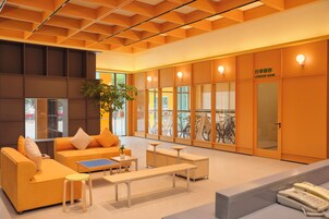 A modern lobby with orange sofas, a coffee table, and a luggage room.