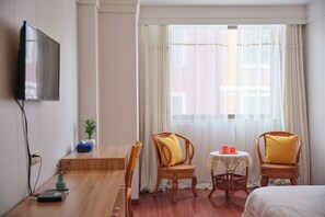 A hotel room with a wooden desk, two wicker chairs with cushions, a small table with a lace tablecloth, and a bed. - Timeless Recreation Hotel (Huanggang)