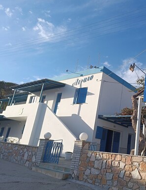 A two-story building with a white facade and blue accents, featuring a staircase and a stone wall. - Aigaio View Studios & Rooms (Syros)