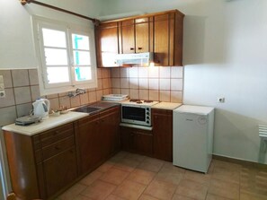 Una cocina con armarios de madera, microondas, lavavajillas y una ventana con persianas.