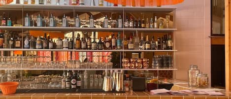 A bar area with shelves of liquor bottles, glasses, and a counter with stools.
