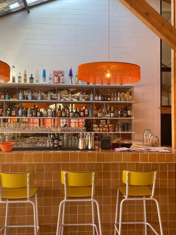 A bar area with shelves of liquor bottles, glasses, and a counter with stools. - La Baignoire Hotel du Golf Lacanau (Lacanau)