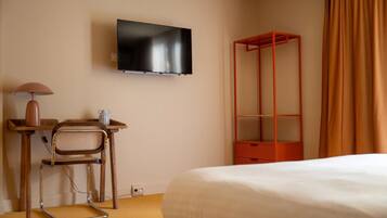 Une chambre d’hôtel comprenant un lit, un bureau avec une chaise, un téléviseur fixé au mur et un meuble de rangement rouge.