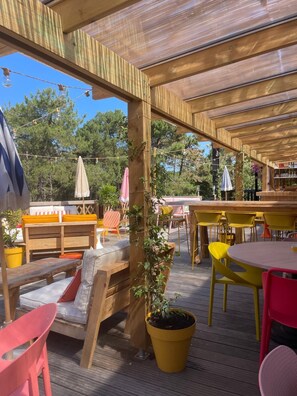An outdoor patio with wooden tables and chairs, a bar area, and potted plants. - La Baignoire Hotel du Golf Lacanau (Lacanau)
