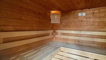 A sauna with wooden walls and benches, a small window, and two wall clocks.