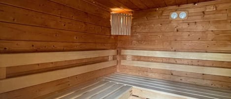 A sauna with wooden walls and benches, a small window, and two wall clocks.