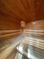 Eine Sauna mit Holzwänden und -bänken, einem kleinen Fenster und zwei Wanduhren.