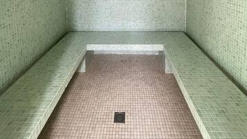 Une pièce carrelée, avec un sol et des murs recouverts de carreaux verts, un luminaire encastré au plafond et un drain au centre.