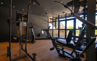 Un gimnasio con equipo de ejercicio, ventanas amplias y piso de madera.