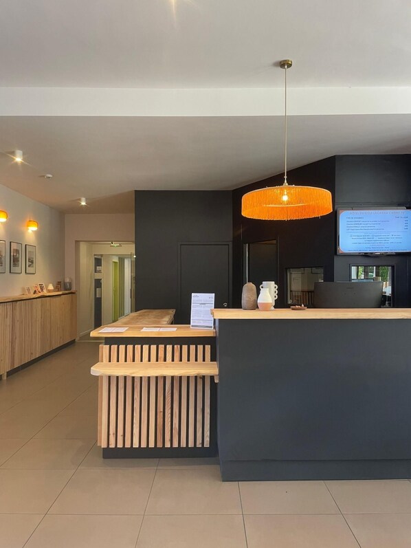 A hotel reception desk with a wooden counter, a hanging orange pendant light, and a digital screen displaying room information. - La Baignoire Hotel du Golf Lacanau (Lacanau)