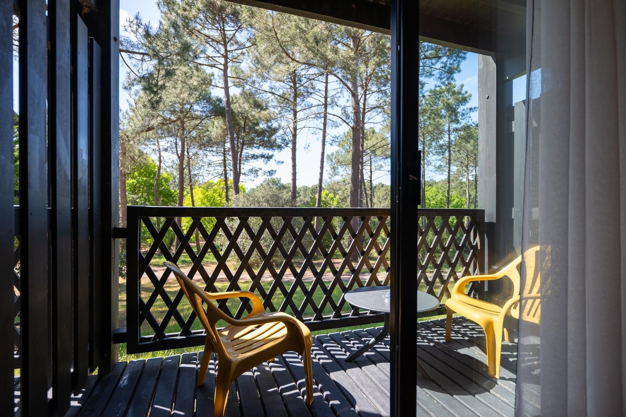 Un espace extérieur abrité, doté d’une terrasse en bois, de deux chaises en plastique jaunes et d’une table.