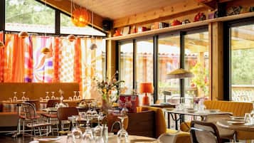 A restaurant with tables set for dining, a large window with curtains, and hanging light fixtures.