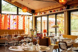 Un restaurante con mesas dispuestas para comer, un ventanal con cortinas y lámparas colgantes.