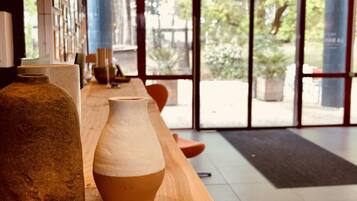 Un comptoir d’accueil en bois agrémenté d’un vase et d’une sculpture en pierre, de grandes fenêtres offrant une vue sur la verdure et des lampes suspendues.