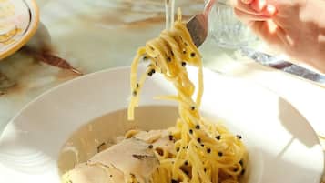 Une assiette de spaghettis avec des boulettes de viande et du poivre noir, une fourchette soulevant quelques spaghettis, et un verre à vin en arrière-plan.