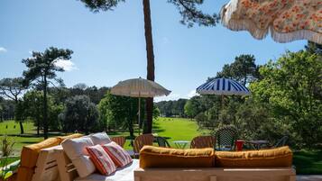 Une terrasse avec des meubles d’extérieur, deux parasols et une vue sur un terrain de golf.