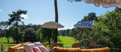 Une terrasse avec des meubles d’extérieur, deux parasols et une vue sur un terrain de golf.