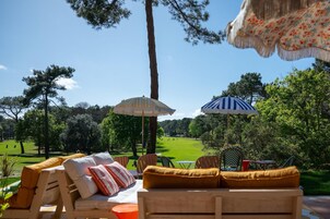 Un patio con mobiliario exterior, dos sombrillas y vistas a un campo de golf.