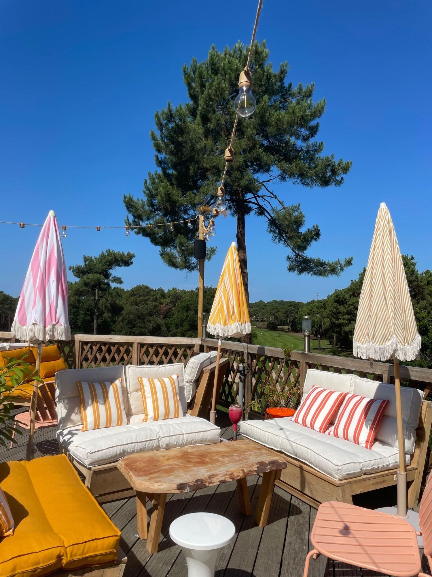 Eine Terrasse mit Gartenmöbeln, darunter eine Sitzecke, Stühle und ein Tisch, umgeben von Sonnenschirmen.