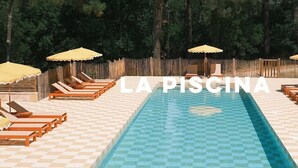 Une piscine entourée d’une clôture en bois, avec des chaises longues et des parasols.
