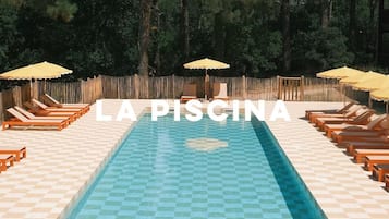 Une piscine entourée d’une clôture en bois, avec des chaises longues et des parasols.