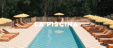 Piscina con sillas de descanso y sombrillas, rodeada por una valla de madera.