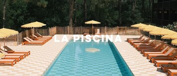 Piscina con sillas de descanso y sombrillas, rodeada por una valla de madera.