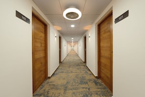 A hotel hallway with wooden doors, numbered room signs, and a patterned carpet.