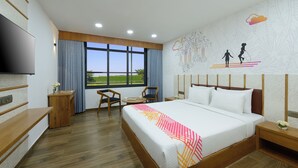 Quarto de hotel com uma cama grande, televisão, secretária, cadeira e vista para o exterior.