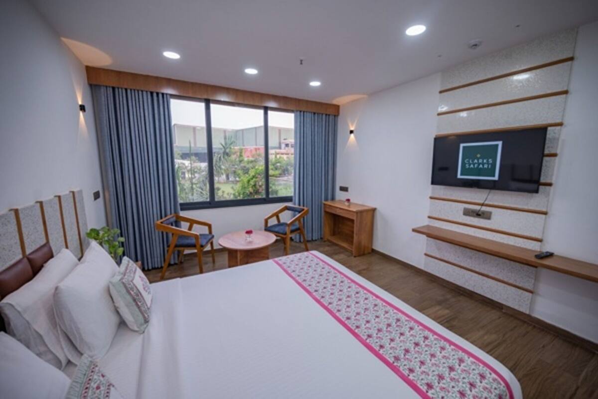 Ett hotellrum med en stor säng, en tv som är monterad på väggen, ett litet bord och ett fönster med gardiner.