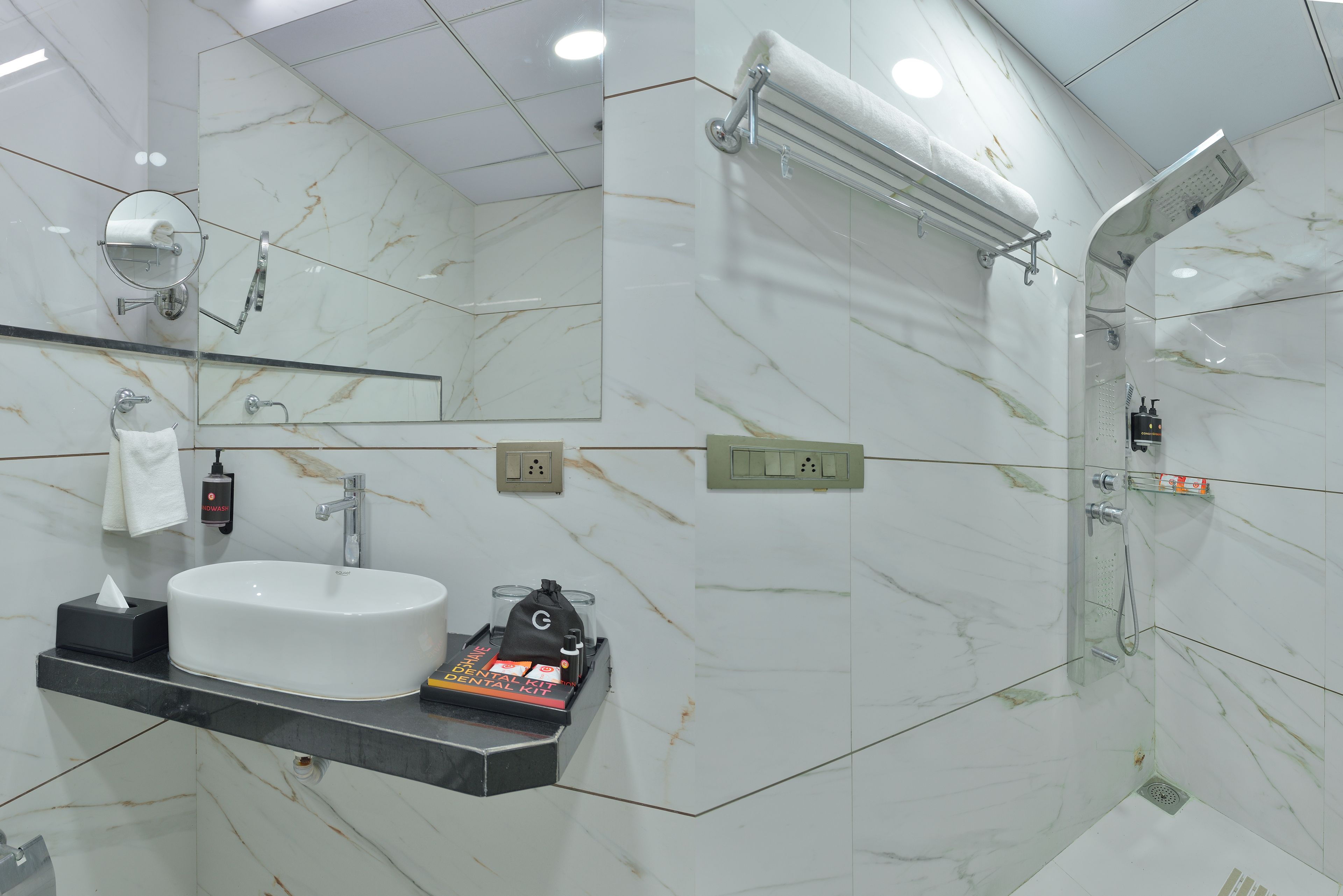 Un baño moderno con lavamanos de mármol blanco, ducha de mano y cabina de ducha con mampara de vidrio.