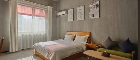 A modern bedroom with a large bed, a green sofa, and a wooden bench. There are wall-mounted air conditioning units and artwork on the walls.
