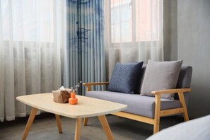 Una sala moderna con un sofá gris, sillones de madera y una mesita con un dispensador de pañuelos y un recipiente naranja.