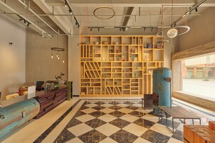 A modern interior with a checkered floor, wooden shelving with various items, a desk with a computer, and a large window.