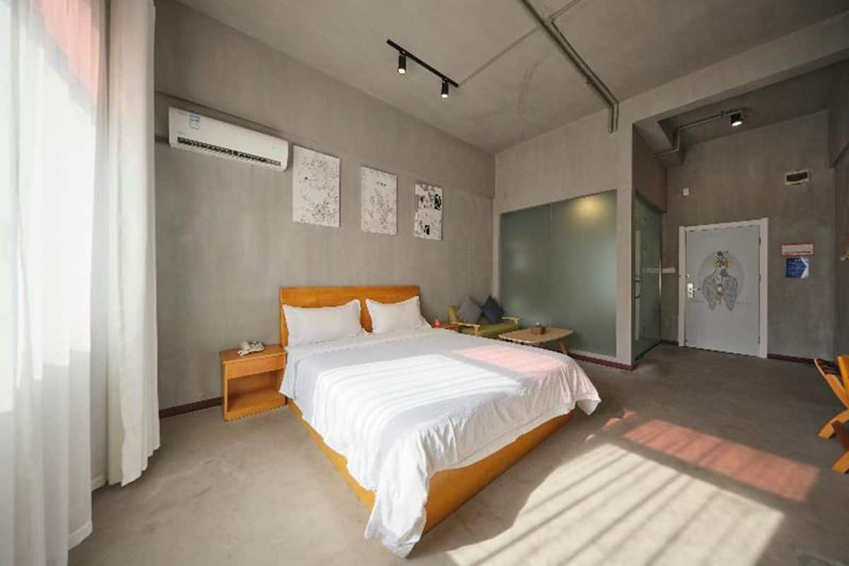 Ein modernes Hotelzimmer mit einem großen Bett, Nachttischen, einer Klimaanlage und einer Glastür zu einem weiteren Raum.