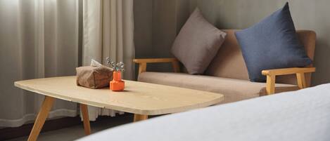 Une pièce avec une table en bois, un canapé beige agrémenté de coussins bleus et bruns, et une fenêtre ornée de rideaux légers.