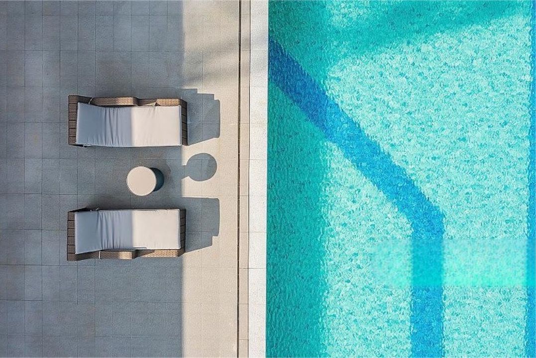 Luftaufnahme eines Poolbereichs mit zwei Liegestühlen und einem runden Tisch.
