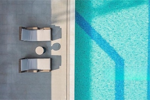Vista aérea de uma área de piscina com duas espreguiçadeiras e uma mesa redonda.