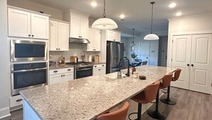 Una cocina moderna con armarios blancos, electrodomésticos de acero inoxidable, encimera de granito e iluminación colgante.