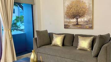 A living room with a grey sofa, a wooden coffee table, a painting of a tree, and a ceiling fan.