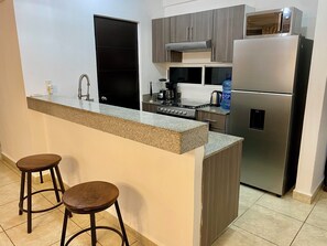 Uma cozinha moderna com uma ilha central, dois bancos altos, uma geladeira de aço inoxidável e um micro-ondas sobre o fogão.