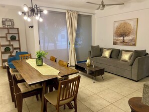 Uma sala de estar moderna com uma mesa de jantar de madeira, cadeiras, um sofá cinzento e um ventilador de teto.