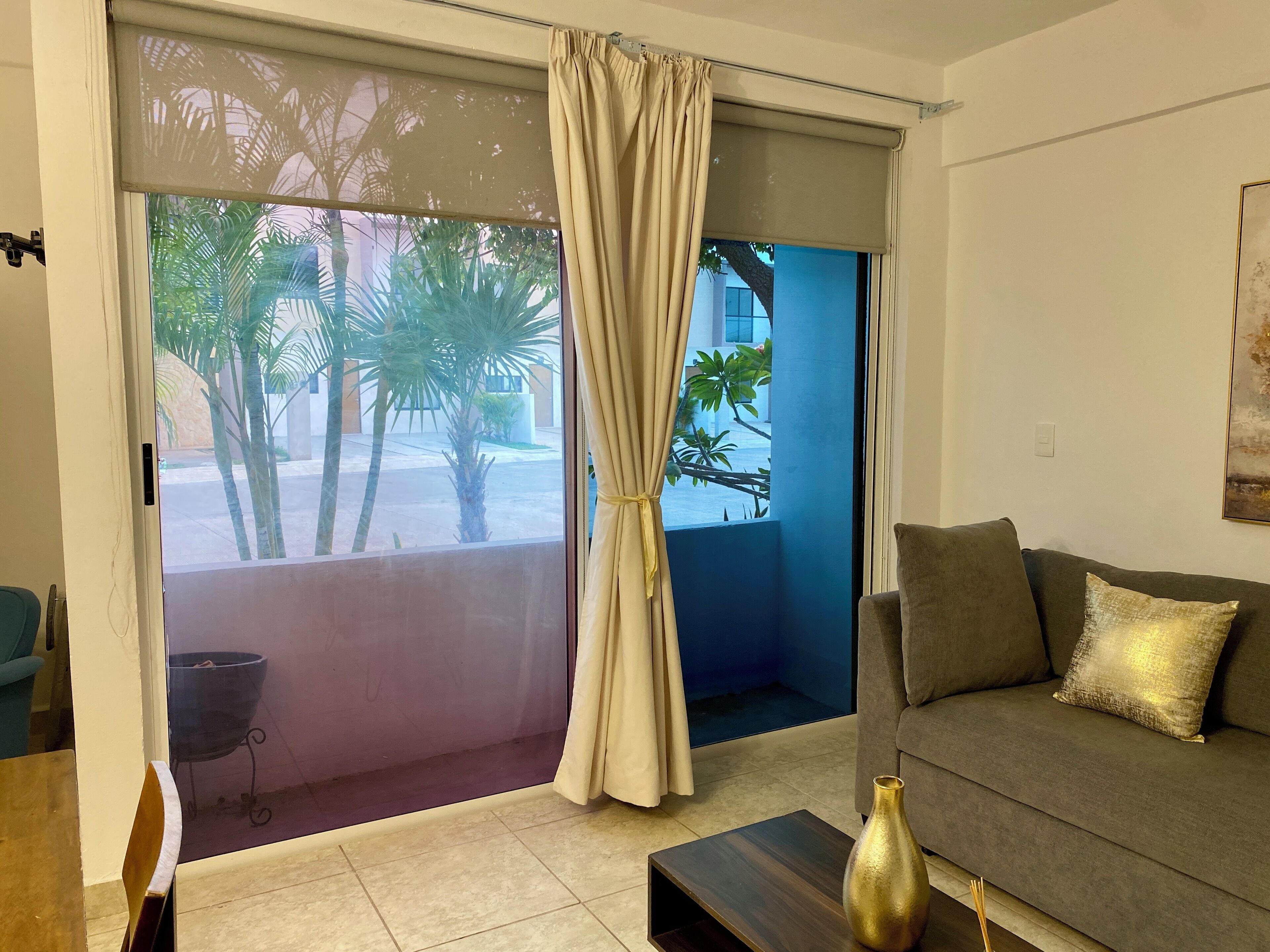 A living room with a sofa, a coffee table, and a view of palm trees outside.