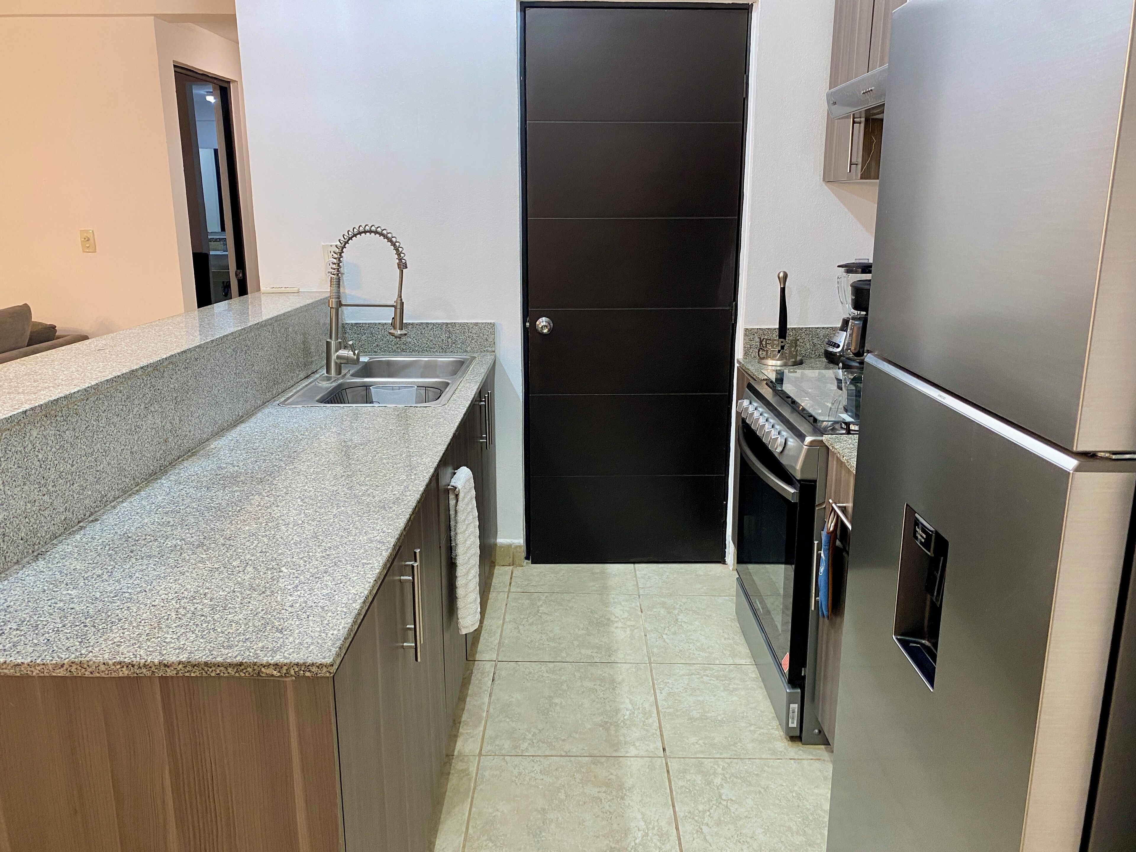 A modern kitchen with granite countertops, stainless steel appliances, and a black door.