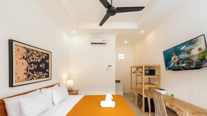 A hotel room with a bed, a desk, and a chair. There is a painting on the wall and an air conditioning unit. - Canggu Surf Paradise (Canggu)
