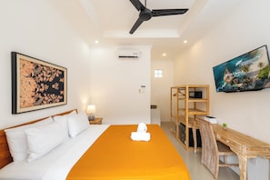Une chambre d’hôtel avec un lit, un bureau et une chaise. Il y a un tableau au mur et un appareil de climatisation.