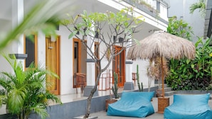 A poolside area with a thatched umbrella, blue bean bags, and potted plants. - Canggu Surf Paradise (Canggu)