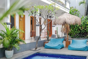 Un espace aménagé au bord de la piscine, avec un parasol en chaume, des poufs bleus et des plantes en pot.