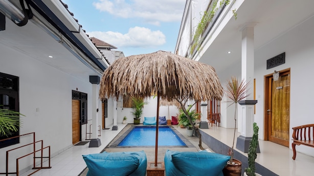 A pool area with a thatched umbrella, blue cushions, and potted plants. - Canggu Surf Paradise (Canggu)